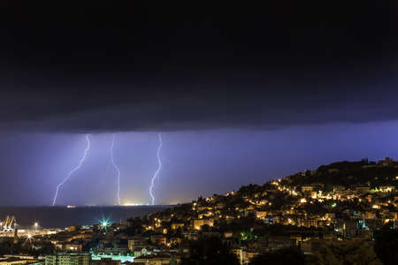 Massive cloud to ground lightning bolts hitting the horizon of city lightsの写真素材