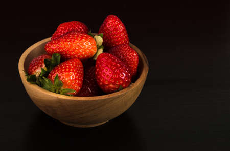 Fresh red strawberries in a wooden bowl on dark wooden backgroundの写真素材