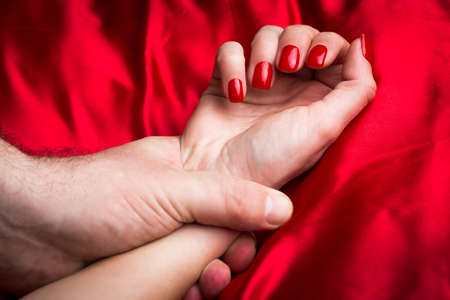 Young couple holding hands sensually on red silk bed.の写真素材