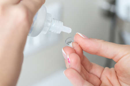 Contact lens on finger and bottle of solution close-up