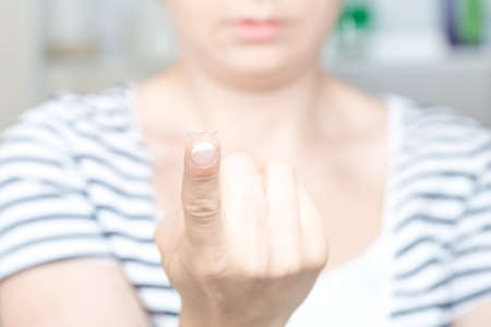 Young woman holding contact lens on finger in front of her eye.  Selective focus on lens.の写真素材