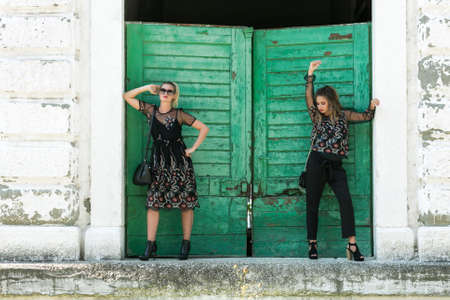 Two happy smiling stylish fashionable girl with blonde long hair,  elegant black dress and modern handbag calling with smart phone. Fashion trendy woman conceptの写真素材