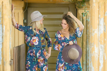 Fashion portrait of two happy woman with blue eyes in flower dress. Fashion hat in a sunny day. Girl with long blonde healthy hair and beautiful smile.の写真素材
