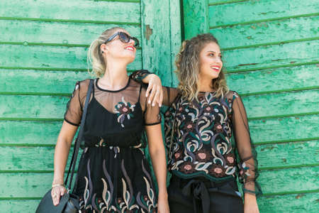 Two happy smiling stylish fashionable girl with blonde long hair,  elegant black dress and modern handbag calling with smart phone. Fashion trendy woman conceptの写真素材