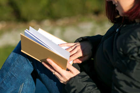 Happy smilling handsome redhead young woman sitting on a small wall and reading a book - Concept...
