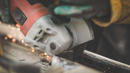 Craftsman sawing metal with disk angle grinder in a warehouse.