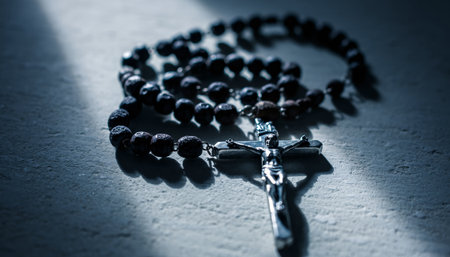 Detailed close-up of traditional rosary featuring rough dark wooden beads and ornate silver crucifix on stone surface. Dramatic lighting creates spiritual atmosphere perfect for religious content.の素材