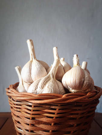 garlic in a brown wicker basket with a gray backgroundの写真素材