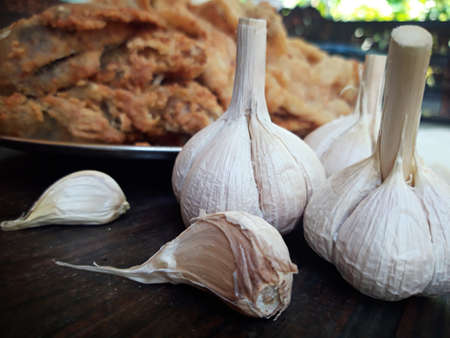 Garlic on a wooden table with a background of food on a plateの写真素材
