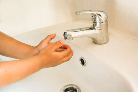 Tiny hands wash hands under the faucet in the sink in the roomの写真素材