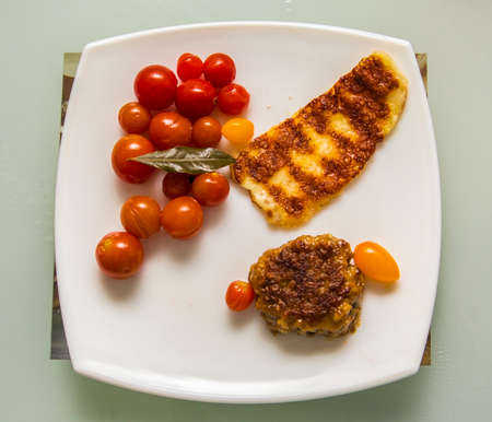 dinner of beef patties grilled cheese and cherry tomatoes on a white plateの写真素材