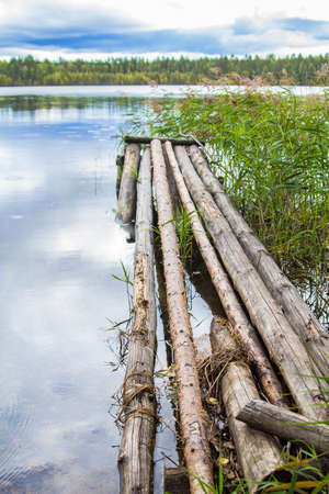 background landscape forest lake under a cloudy sky with old wooden footbridges of logsの写真素材
