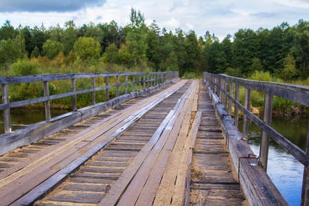 background old rusty destroyed bridge of planks and iron through forest Riverの写真素材