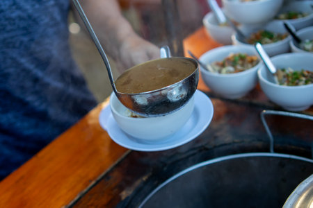 The soto seller is scooping up the soto sauce using a ladleの写真素材