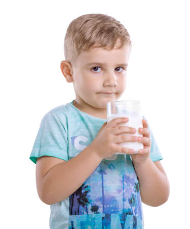 Pensive little child in a blue t-shirt holds a glass of milk. A cute little kid with fresh milk isolated on a white background.の写真素材