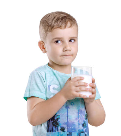 A cute little kid in a blue t-shirt with a glass of delicious milk. Healthful and organic food and drings. Handsome little boy is holding a full glass of fresh and organic milk isolated on white background.の写真素材