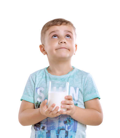 Tiny cute boy wearing in a blue t-shirt is holding a full glass of milk and dreaming. Charming young baby boy with fresh milk  isolated on a white background.の写真素材