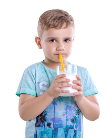 Pretty little boy is drinking a glass full of milk from yellow straw isolated on a white  blackground. A cute little child holds a glass of milk on gray background. Healthy and dairy products.の写真素材
