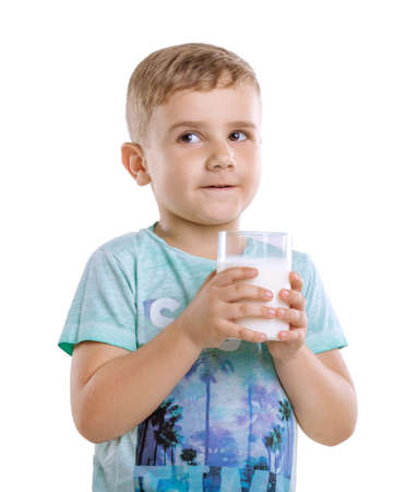 Adorable boy in blue t-shirt is holding glass of milk, isolated on a white background. Beautiful little kid with pretty smile is holding a glass of fresh and organic milk isolated on a white background.の写真素材