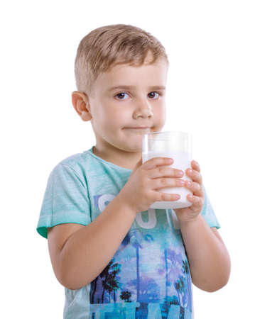 Curious little boy  is drinking nutritious milk in the morning.  A cute child wearing in a blue t-shirt is holding a full glass of milk isolated on a white background.の写真素材