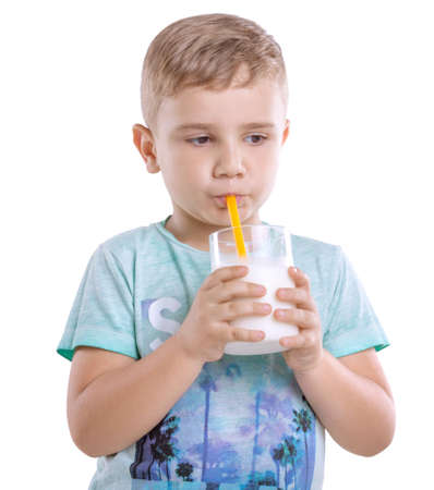 A cute little kid in blue t-shirt with a glass full of nutritious and organic milk isolated on a white background. Pretty little boy is drinking milk from a yelllow straw isolated on a white background.の写真素材
