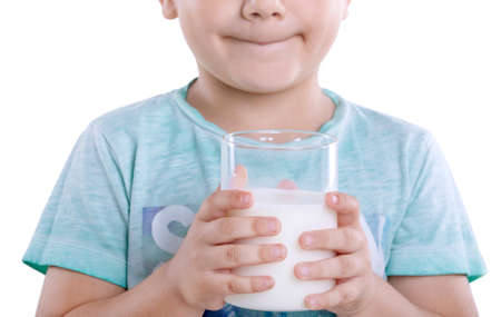 Healthy and delicious milk in a glass in the hands of little boy isolated on a white background. A cute little kid is holding a full glass of fresh milk and looking very happy.  Close-up charming boy with milk.の写真素材