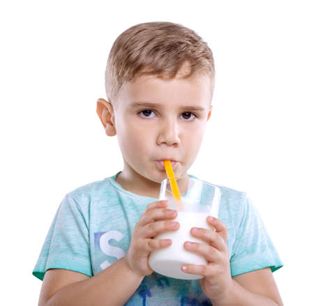 A beautiful little kid in a blue T-shirt with a glass of a tasty milk. Delightful little baby boy is drinking fresh milk from a bright yellow straw. Close-up portrait of amazing boy drinks a glass of milk isolated on white background.の写真素材
