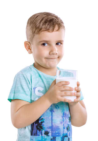 A cute little blonde baby boy in blue t-shirt is holding a glass of organic milk isolated on a white background close-up.の写真素材