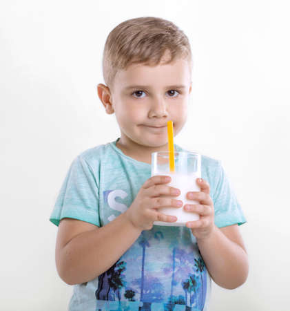 Portrait of a charming little boy who is enjoying delicious milkshake. Cheerful little kid with a glass of organic milk. Smiling boy with milk. Happy little child is holding a glass of organic milk with a yellow straw.の写真素材