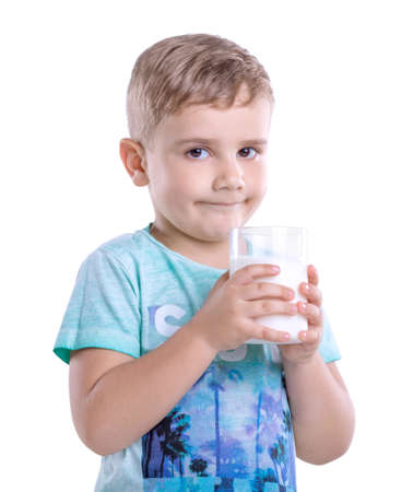 Close-up portrait of amazing boy drinks a glass of milk isolated on white background. Curious little kid wearing blue t-shirt with a glass full of nutritious milk isolated on a white background.の写真素材