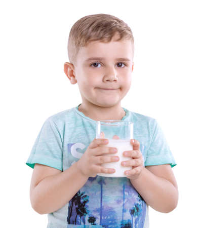 A nice little child in a blue t-shirt with a cup of delicious milk. Healthful and organic food and drings. A cute kid is holding a full glass of fresh and organic milk isolated on white background.の写真素材