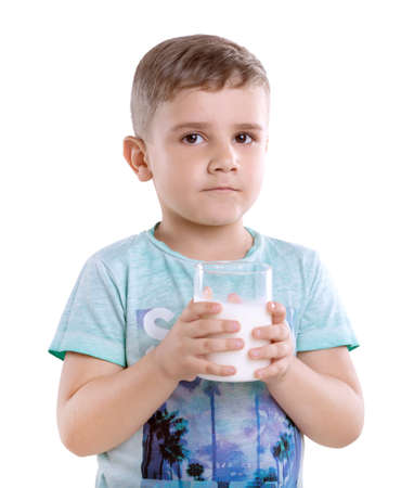 Charming little boy in a blue t-shirt is  holding a glass full of milk, isolated on a white background. Portrait of cute little boy with glass of milk.の写真素材