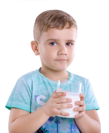 Curious little kid wearing blue t-shirt with a glass full of nutritious milk isolated on a white background. Tiny cute boy wearing in a blue t-shirt is holding a full glass of milk isolated on a white background.の写真素材