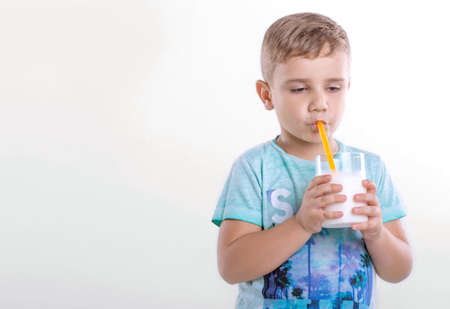 Close-up portrait of charming little boy with a glass full of organic milk on a gray background. A nice little boy holds a glass of fresh milk on gray background. Healthy products. Dairy products.の写真素材