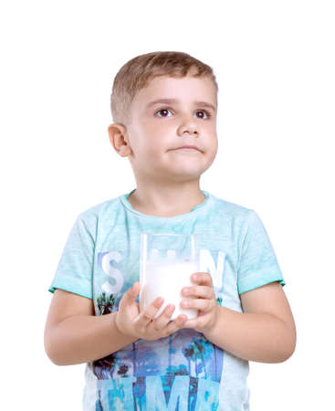 Close-up portrait of a nice little boy with a glass of organic milk isolated on a white background. Beautiful little boy with a glass of milk wondering about it's amazing taste.の写真素材
