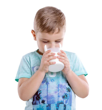 Tiny cute boy wearing in a blue t-shirt is drinking a full glass of milk isolated on a white background. Handsome little boy and organic milk.の写真素材