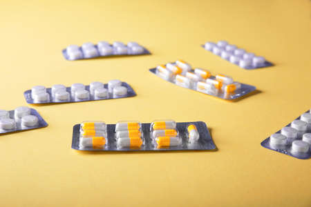 Packaging for drugs: antibiotics, painkillers, vitamins and aspirin tablets. Set of white blisters realistic icons with pills and capsules scattered on a yellow background.の写真素材