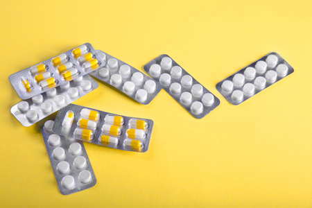 Medicine pills and capsules in blister packaging scattered on a yellow background. Health care concept. White and yellow pills on bright yellow background. Tablets of drug for treatment. Health.の写真素材