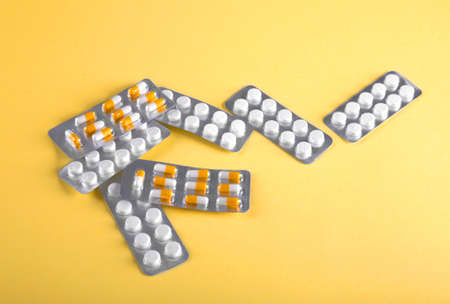 Many different pills, vitamins, tablets, dose, medicine, pilule and drugs on yellow background. Medicinal tablets. White and yellowt pills in packaging are scattered.の写真素材