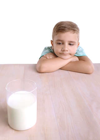 A cute little boy with a transparent glass full of tasty milk filled with vitamins. A wonderfull little kid in a blue T-shirt with a glass of milk and lies on his hands, isolated on a white backgroundの写真素材