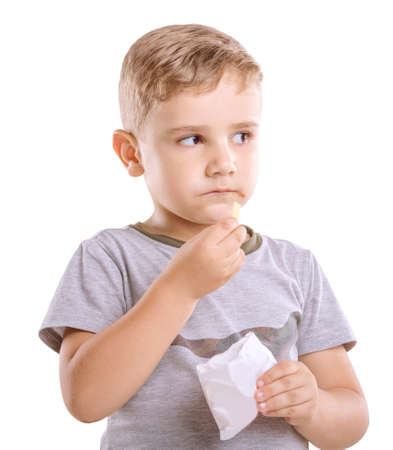 Close-up portret of incredible and cute child is eating flavorful French fries isolated on a white background. Charming little kid dressed in a gray T-shirt is holding a box of food in his hand.の写真素材