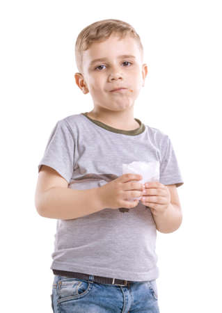 A charming child with eat in his hands isolated on a white  background. The unbelievable boy dressed in a gray T-shirt and blue jeans is holding a box of food in his hands and eating French fries.の写真素材
