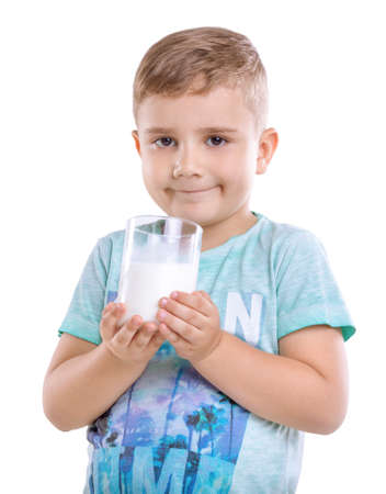 Amazing and cute little boy with blonde hair and in blue t-shirt holds a glass full of organic milk in two hands, isolated on white background.  Charming baby boy with healthy, organic and fresh milk.の写真素材
