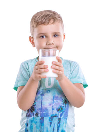 Close-up portrait of a small cute boy holding a glass of delicious milk. An incredibly beautiful child is wearing a blue T-shirt with patterns. A small boy holds a large glass of milk and smiles.の写真素材