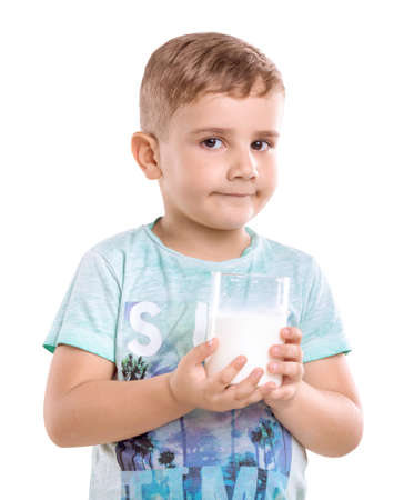 Charming boy with blonde hair holds a glass full of organic milk and looks cute,  isolated on a white background. The pretty smiling little kid is standing and holding a glass of fresh milk.の写真素材