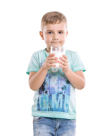 Close-up portrait of a little handsome kid holding a glass of delicious milk.  A small child is wearing a blue T-shirt with patterns and holds a large glass of milk and smiles.の写真素材