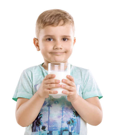 Close-up portrait of a cheerful child holding a glass of tasty milk isolated on a white background.  A pretty boy is wearing a blue T-shirt with patterns and holds a large glass of milk and smiles.の写真素材