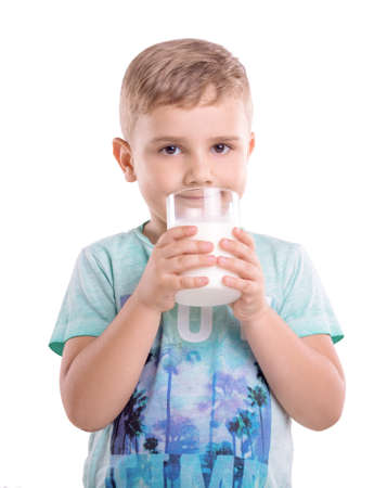 Close-up portrait of a little cheerful child with dimples on his cheeks holding a glass of fresh milk.  A smiling boy is wearing a blue T-shirt with patterns and holds a large glass of milk.の写真素材