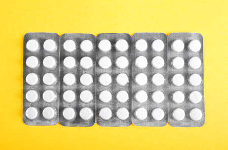 Different packagings of white pills and tablets. Prescripted medicinal drugs on a bright yellow...