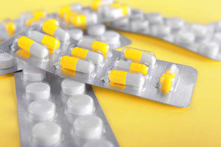 Close-up various packagings of orange and white tablets and capsules. Pills on a bright yellow background. Medical supplements: painkillers, antibiotics, drugs.の写真素材